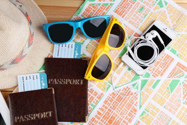 Image of passports, tickets, colourful sunglasses, earphones and smart phone placed on top of a paper map of a city.