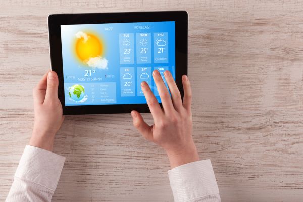 Image of a tablet screen displaying information on weather forecast with hand hovering over the screen.