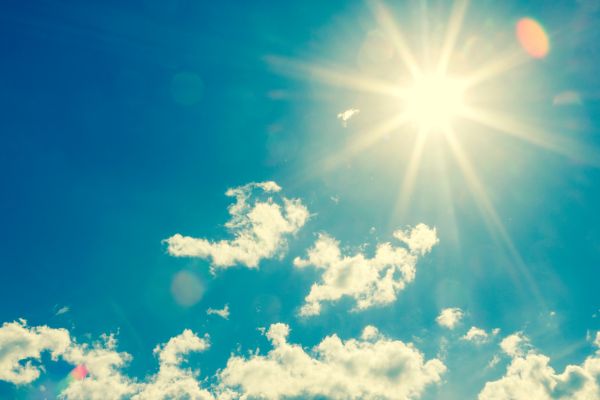 Image of sun shining in a blue sky with little cloud.