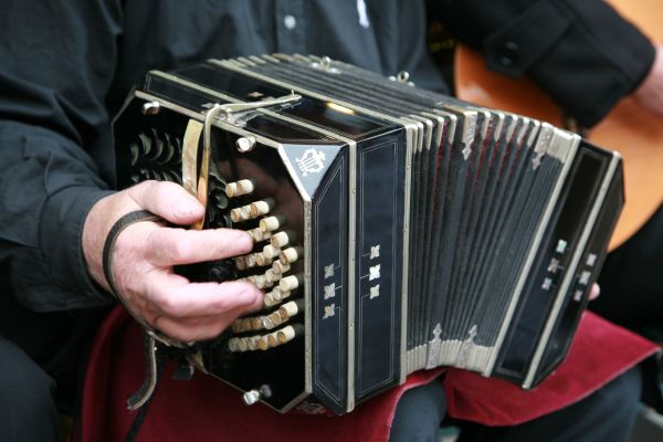 Close-up of a bandoneon being played, a key instrument in traditional Argentine tango music, with fingers pressing the buttons and bellows extended.