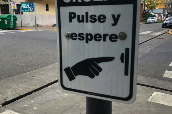 A yellow pedestrian crossing button at a Buenos Aires intersection, mounted on a pole next to a traffic light.