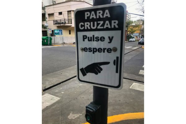 A yellow pedestrian crossing button at a Buenos Aires intersection, mounted on a pole next to a traffic light.