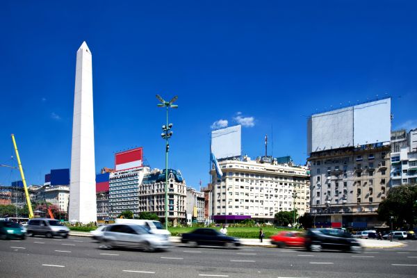 Daytime traffic speeding past El Obelisco in Buenos Aires, showcasing the hustle and energy of the city center.